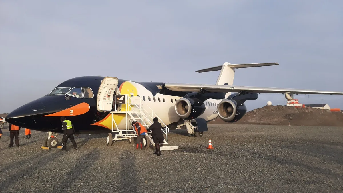 Black, white, and yellow aircraft on the ground with people around and clear sky background.