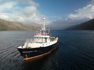 Antarctic research ship navigating icy waters under a cloudy sky.