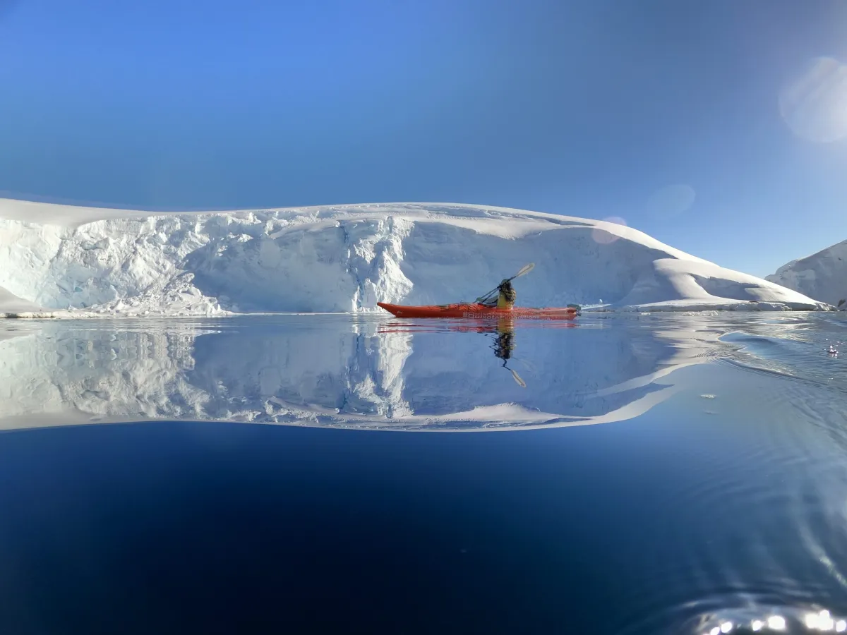 Serene icy landscape with calm water reflecting snowy mountains and a red kayak.