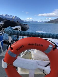 Antarctic research ship Hans Hansson with lifebuoy and scenic fjord background.