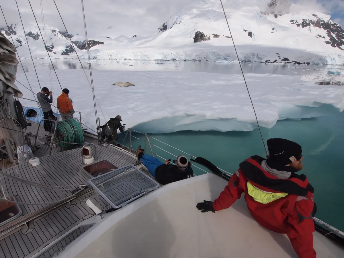 "People on boat exploring icy waters with snow-covered mountains and icebergs in background.