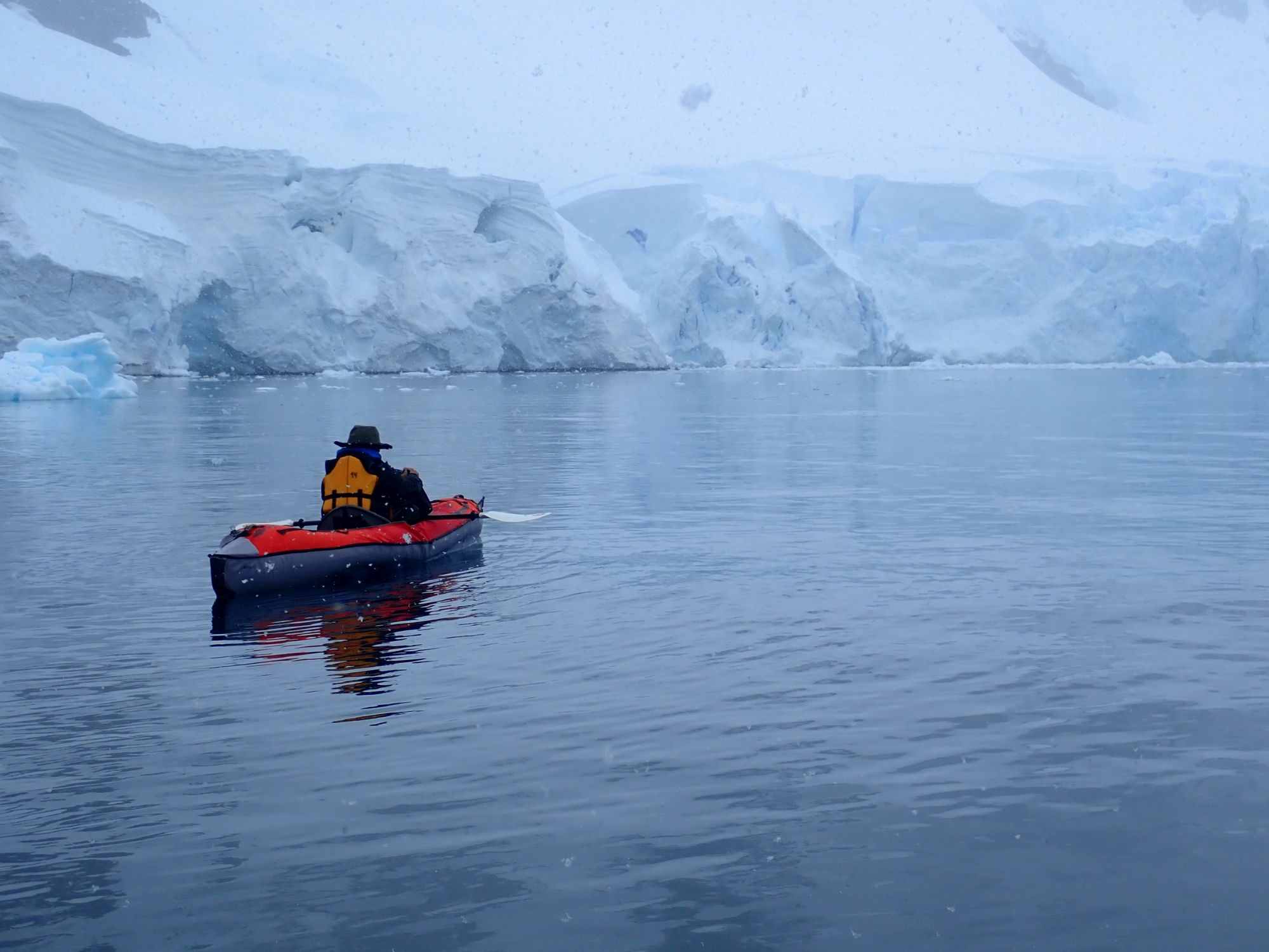 Person in a red and black kayak paddling in calm waters, surrounded by large ice formations and glaciers in Antarctica.