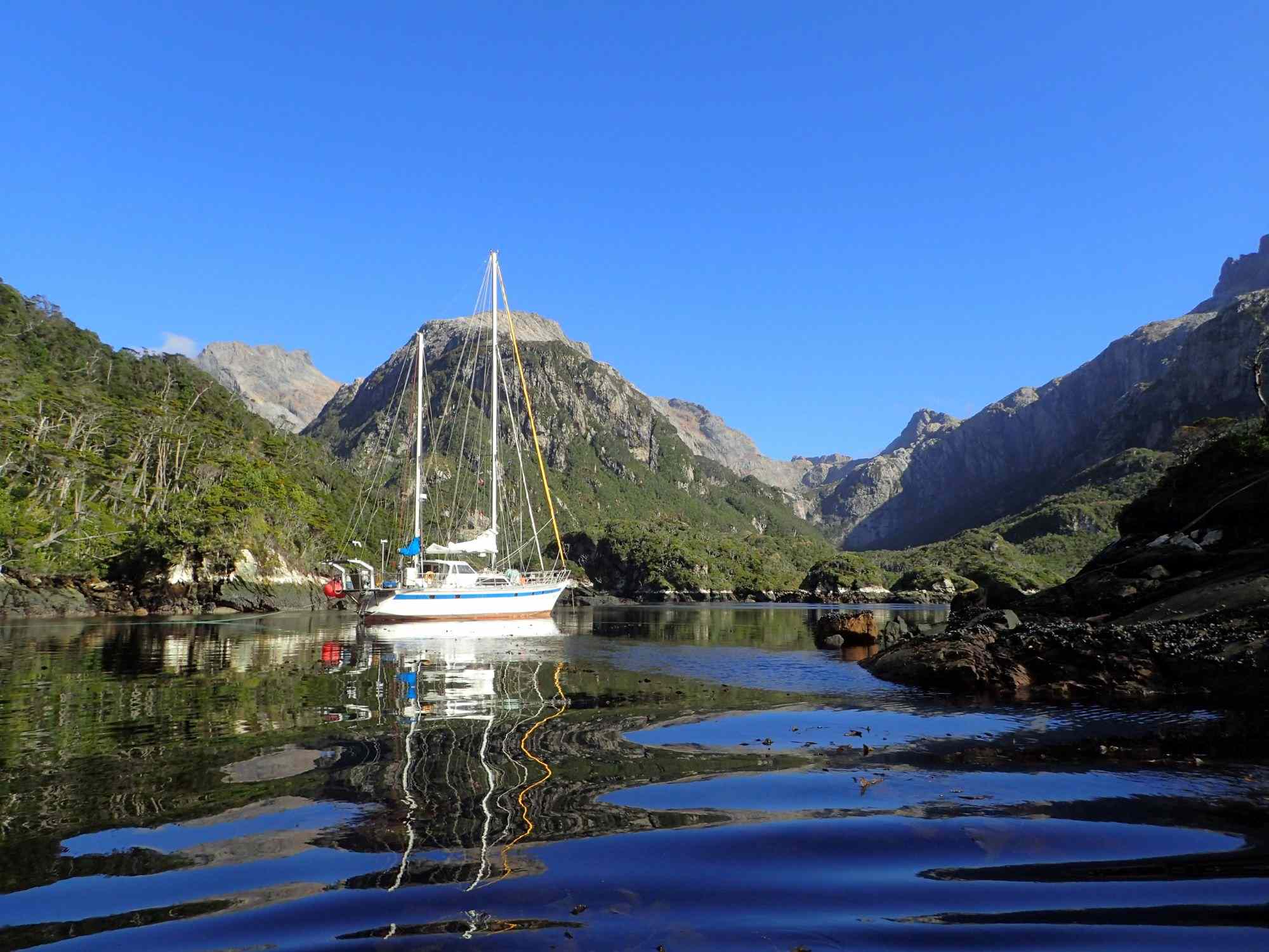 Sailboat anchored in calm Antarctic waters, surrounded by mountainous terrain, reflecting the serene landscape