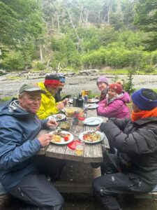 Group of travelers with Quixote Expeditions enjoying a scenic outdoor meal by the forest during an Ocean Tramp expedition