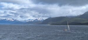 Sailboat navigating icy waters of Antarctica with snowy mountains and cloudy sky in the background.